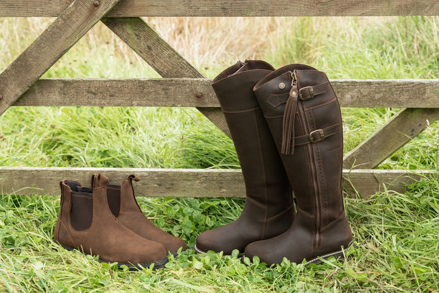 Short and tall brown country and yard boots beside a wooden gate