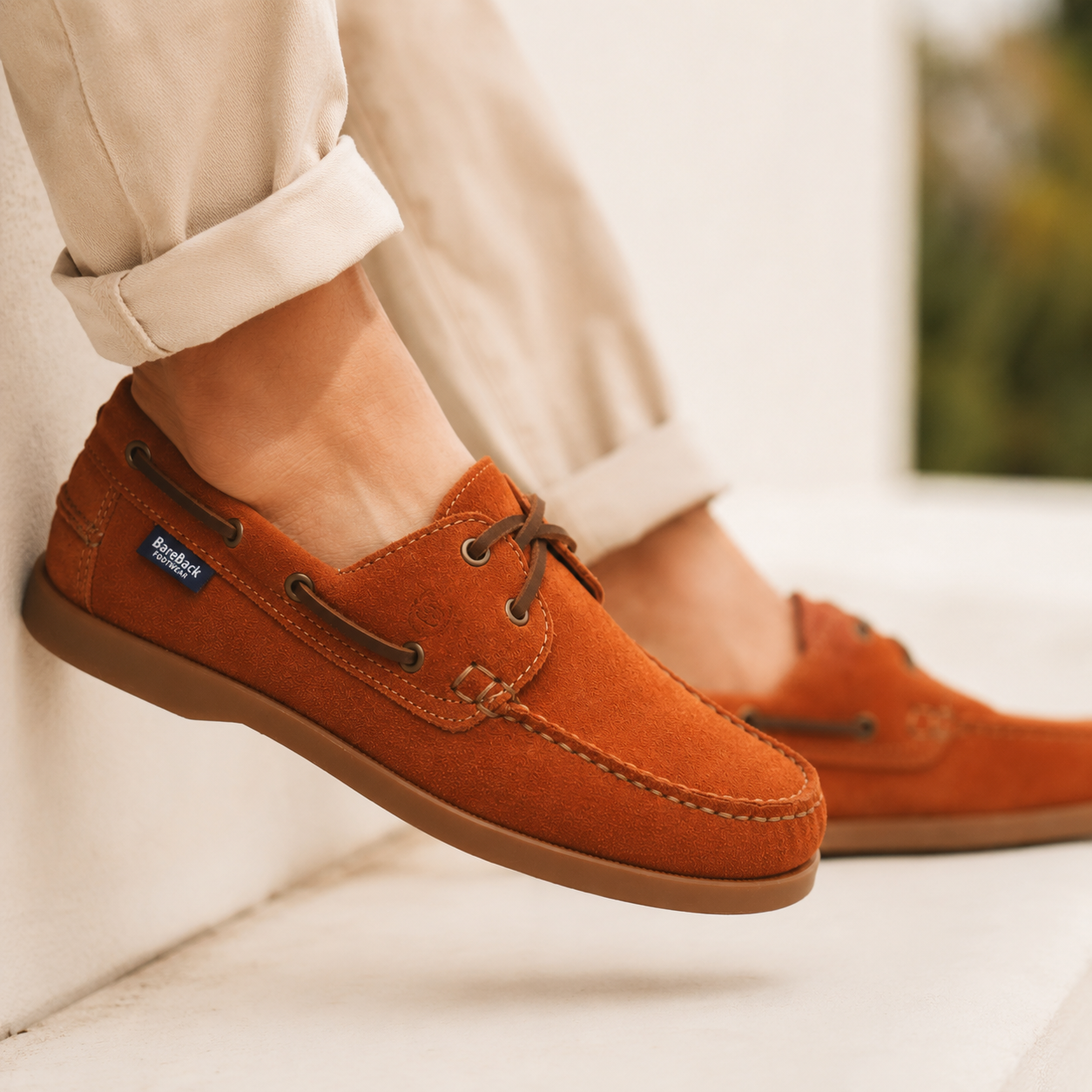 Brown suede shoes worn with light-colored pants on a blurred background