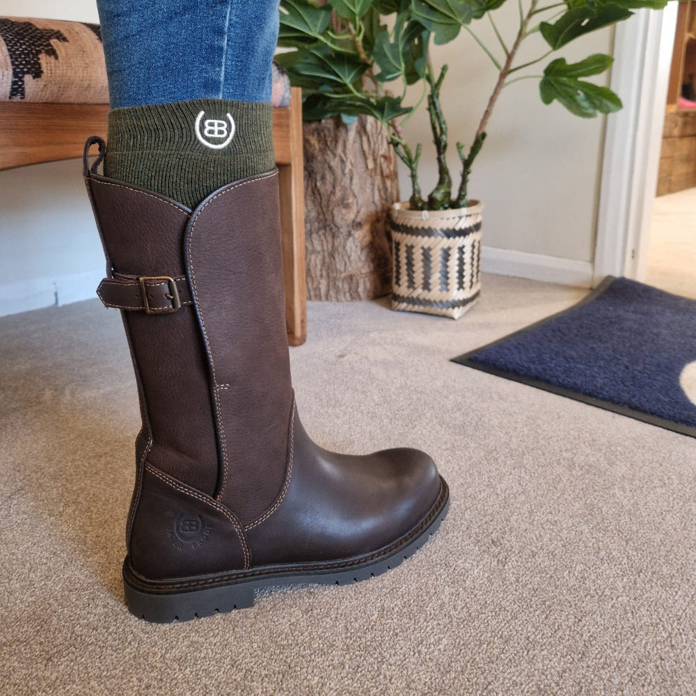 Brown riding boot worn with a sock featuring a logo, indoors.